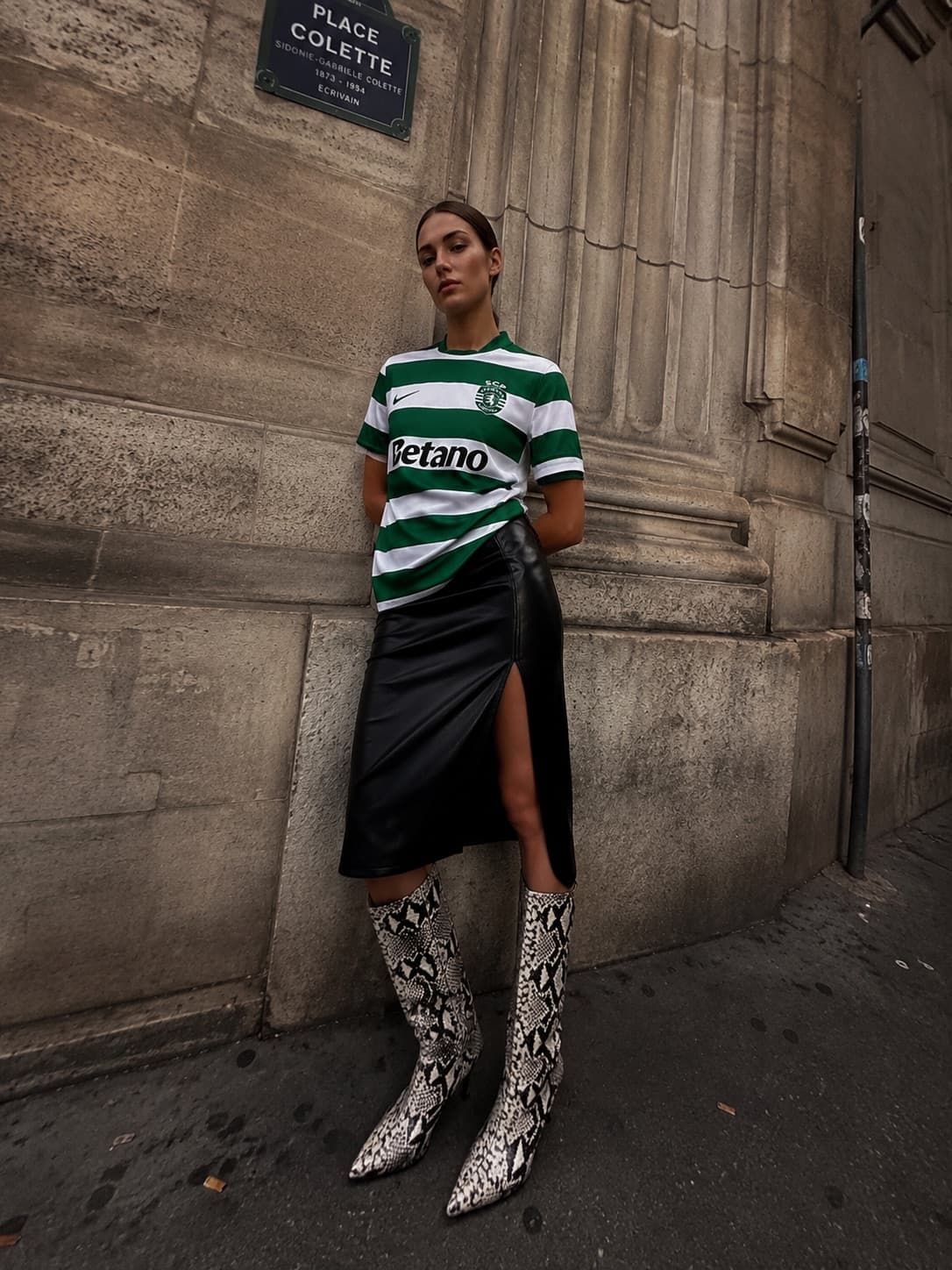 Maglia dello Sporting, gonna in pelle nera con spacco e stivali pitonati, appoggiata al muro di pietra di Place Colette.